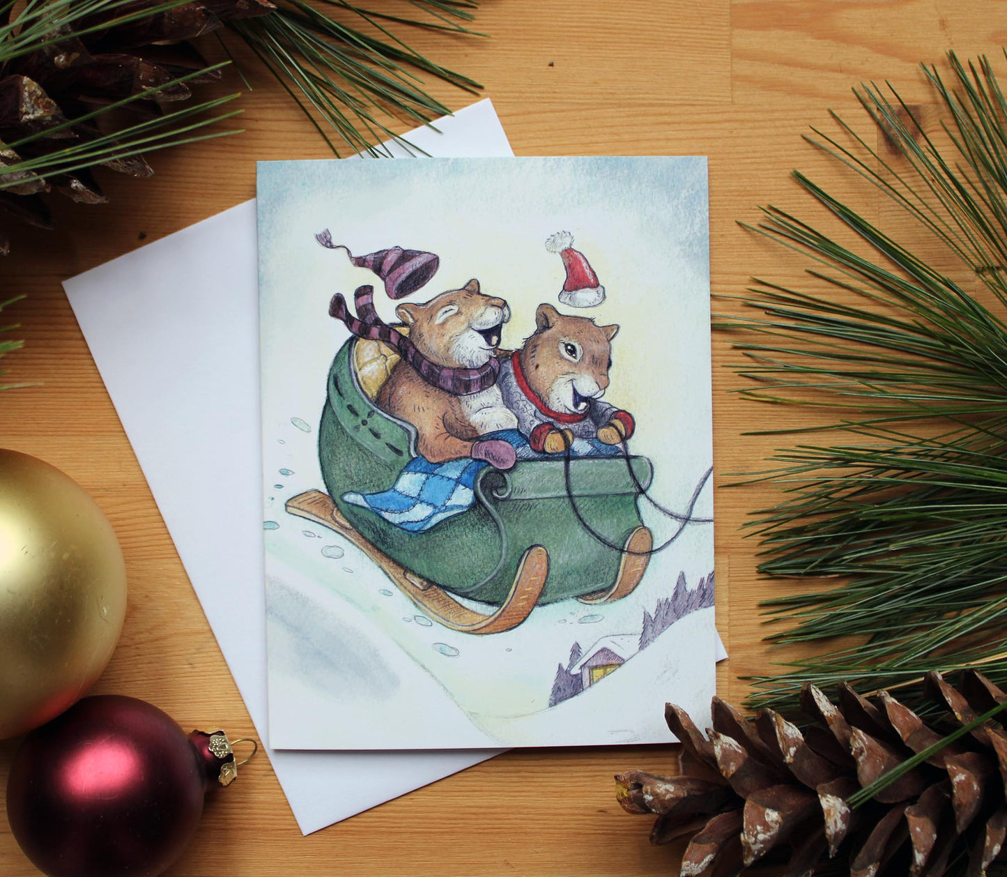 Illustrated chritmas card of two little red squirrels laughing in a sleigh.