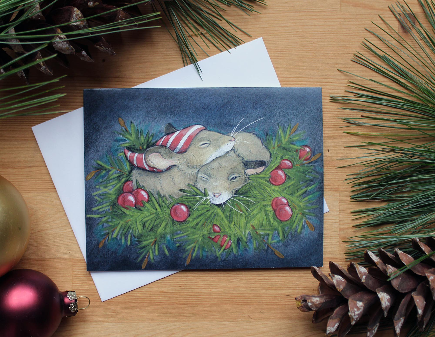 Illustrated christmas card of two sleepy mice cuddling together  on a bed of pine needles and red berries.