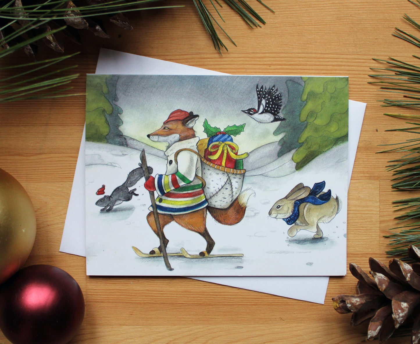 illustrated christmas card of fox wearing a Hudson Bay Coat and travelling with gifts carried in a birch bark basket on his back. Rabbit, squirrel and woodpecker join him on his journey.
